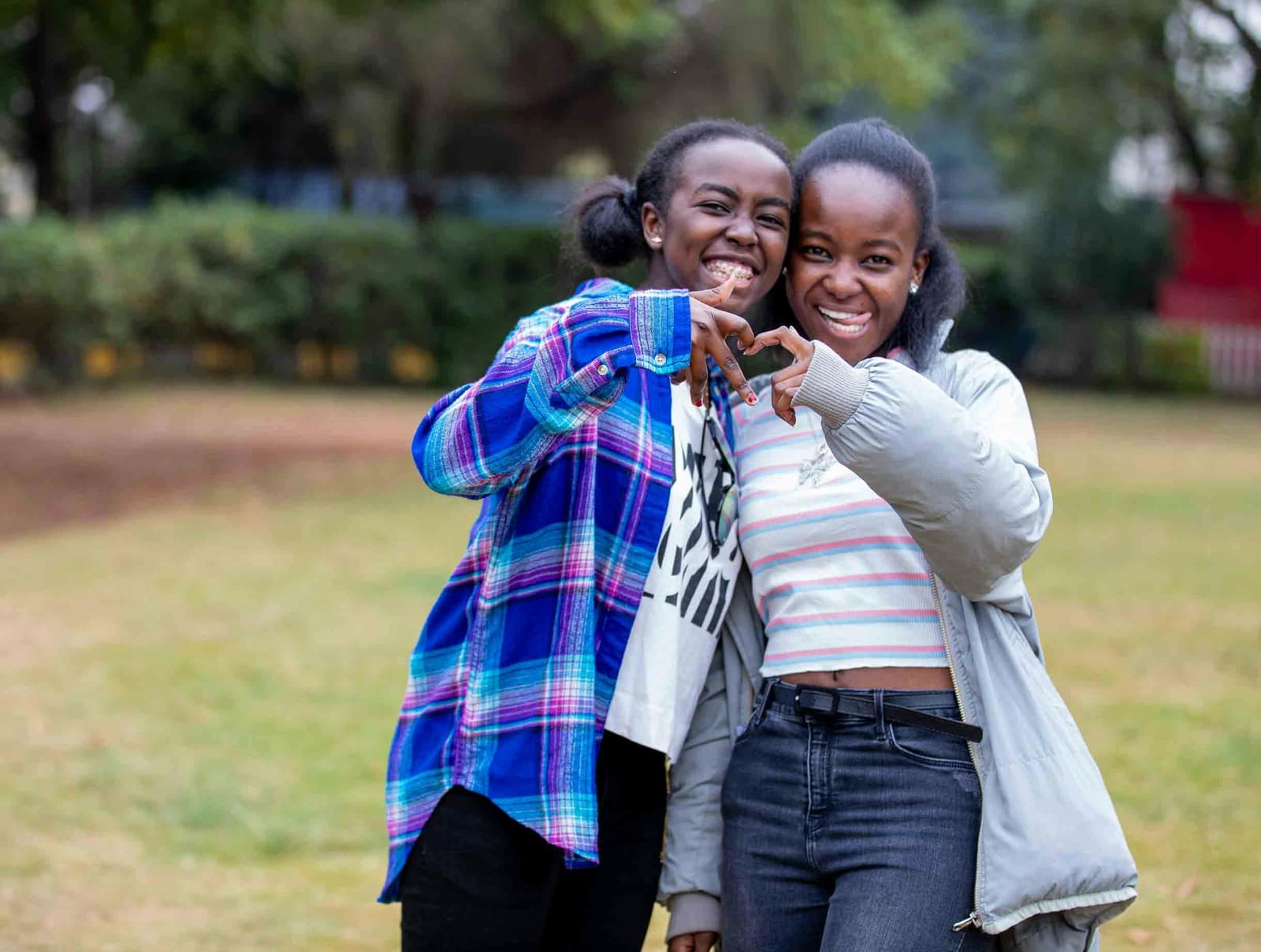 Two teenagers forming a heart shape with their hands in a park