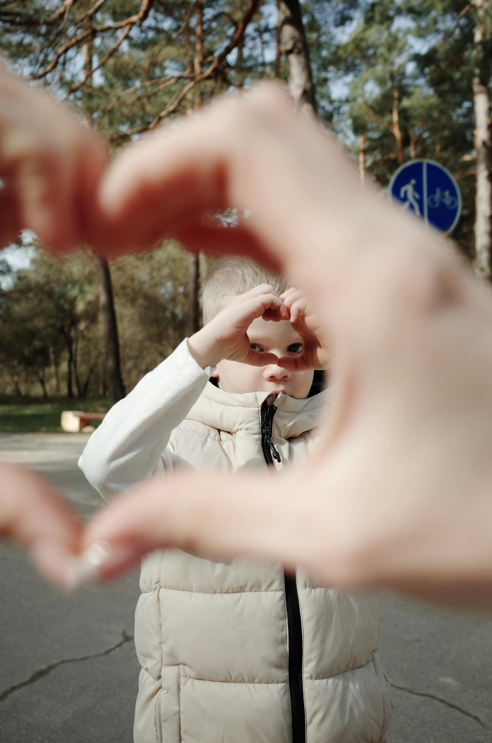 A young child forming a heart shape with their hands outdoors